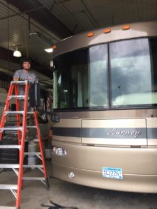 A man standing on top of a ladder next to a bus.