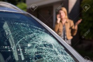 A woman on the phone while looking at a car windshield.